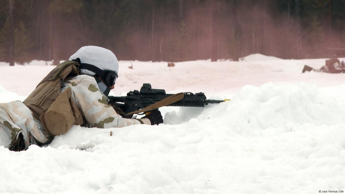 Soldado deitado em neve, com arma, em posição de tiro