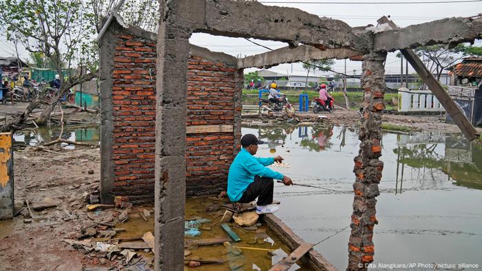 A man fishes in water inundating the area around an abandoned building due the rising sea levels and land subsidence in Sidogemah, Central Java