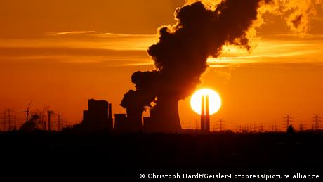Smoke billows from a power station against a red sky and setting sun