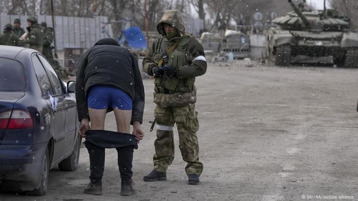 Ukraine Krieg mit Russland | Mariupol: Ein Mann an einem Checkpoint mit heruntergelassener Hose vor einem Soldaten 