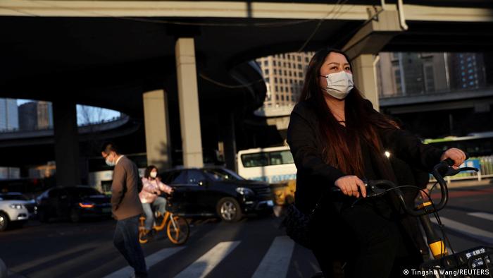 Eine Frau radelt mit medizinischer Maske durch Peking