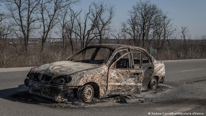 A burned out car riddled with bullet holes 