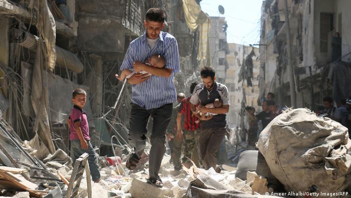 Syrian men with babies make their way through the rubble of destroyed buildings 