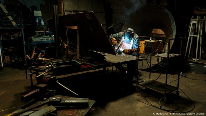 A metalworker welds an anti-tank obstacle in a dark studio