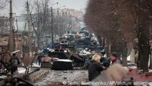People look at the gutted remains of Russian military vehicles on a road in the town of Bucha, close to the capital Kyiv, Ukraine, Tuesday, March 1, 2022. Russia on Tuesday stepped up shelling of Kharkiv, Ukraine's second-largest city, pounding civilian targets there. Casualties mounted and reports emerged that more than 70 Ukrainian soldiers were killed after Russian artillery recently hit a military base in Okhtyrka, a city between Kharkiv and Kyiv, the capital. (AP Photo/Serhii Nuzhnenko)