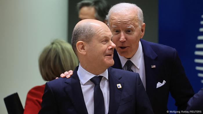US President Joe Biden speaking to a smiling German Chancellor Olaf Scholz and tapping himo on the shoulder during a European Union leaders summit amid Russia's invasion of Ukraine, at the EU headquarters in Brussels, Belgium March 24, 2022