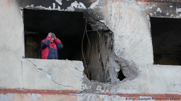 Man holds his head as he looks out of a destroyed house
