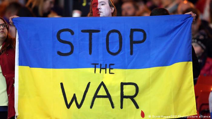Foto de una persona que sostiene una bandera de Ucrania con las palabras Detengan la guerra.