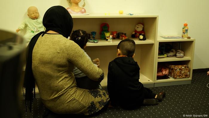 Woman and two children in a room, a baby doll and some stuffed animals