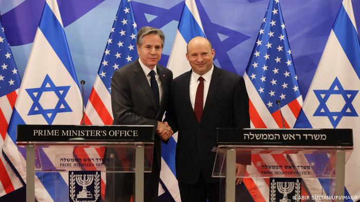 Blinken und Bennett shaking hands, the US and Israeli flags behind them