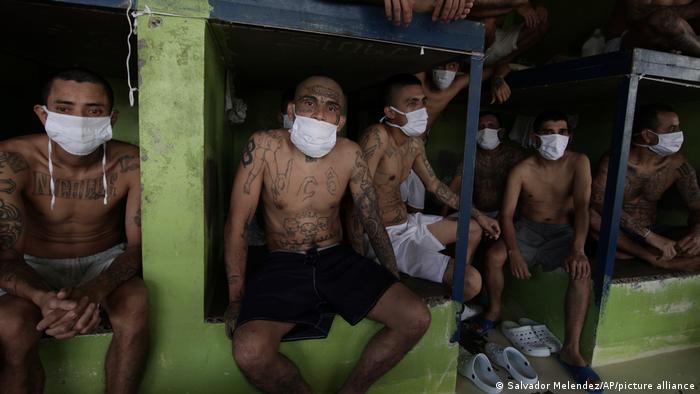 Imprisoned gang members, wearing protective face masks, sit inside a group cell