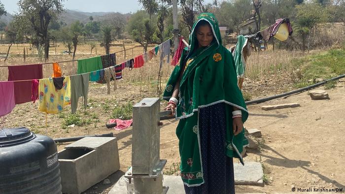 A Garasiya woman operating a water pump as clothes hang out to dry behind her