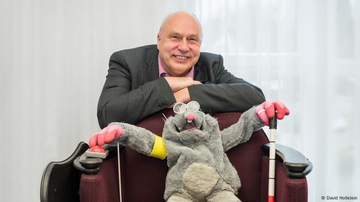 Stefan Wilke hockt hinter einem Sessel in dem eine Handpuppe sitzt