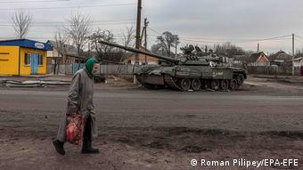 Пожилая женщина в городе Тростянец на фоне танка