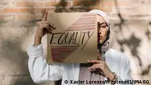 IMAGO Creative: Frauenmonat, Feministischer Aktivismus Young woman covering face with placard in front of wall on sunny day model released Symbolfoto property released XLGF01575