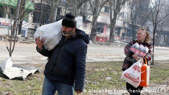 Local residents carry foodstuff while walking past an apartment building damaged during Ukraine-Russia conflict in the besieged southern port city of Mariupol