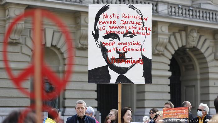 Demonstrators hold up a sign showing Putin's face and names of European companies