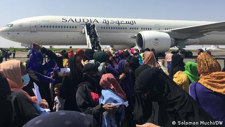 Hundreds of people stand on the airport tarmac in front of a Saudia plane