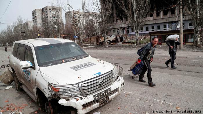 Men walk past an OSCE car damaged in the course of Russia's war in Ukraine in Mariupol
