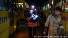 TOPSHOT - A man carries a child as a convoy of 30 buses carrying evacuees from Mariupol and Melitopol arrive at the registration center in Zaporizhzhia, on April 1, 2022. - Late on April 1, people who managed to flee Mariupol to Russian-occupied Berdiansk were from there carried on dozens of buses to Zaporizhzhia, some 200 kilometers (120 miles) to the northwest, according to an AFP reporter on the scene. (Photo by emre caylak / AFP) (Photo by EMRE CAYLAK/AFP via Getty Images)