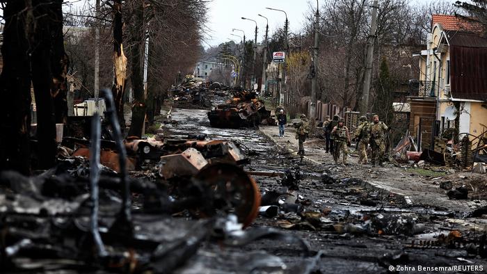 Soldiers walk past a destroyed Russian tank and armored vehicles in Bucha, Ukraine