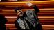 Jon Batiste wears a cape and smiles at the camera on stage at the Grammys. Jon Batiste wears a cape and smiles at the camera on stage at the Grammys.