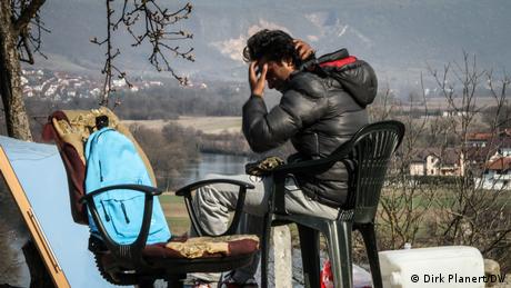 Čovjek sjedi na plastičnoj stolici s rijekom ili jezerom i planinama u pozadini