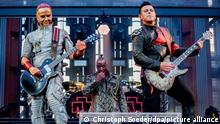 Drei Bandmitglieder von Rammstein auf der Bühne, in der Mitte Frontmann Till Lindemann, links Paul Landers, rechts Richard Kruspe. 