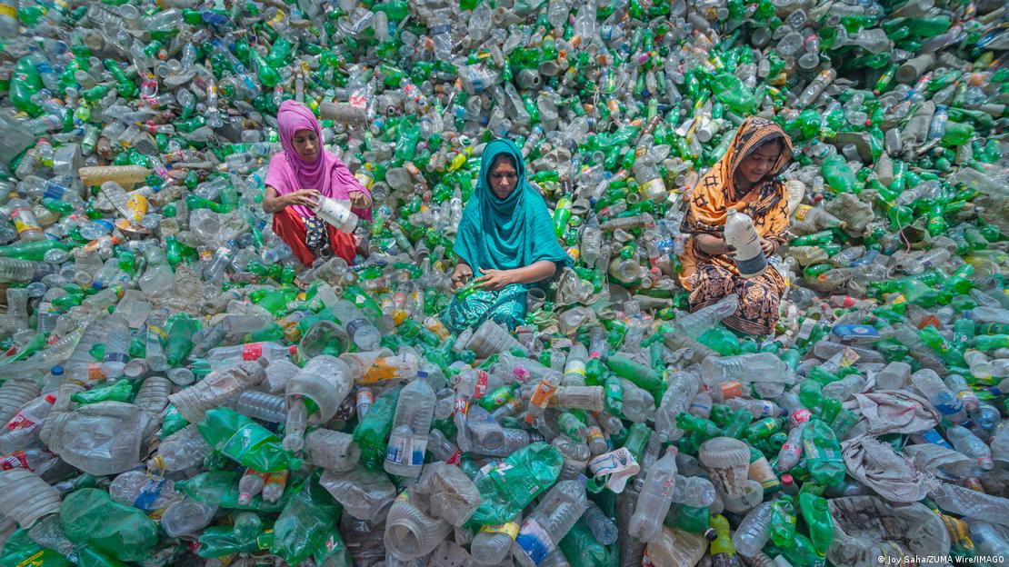 Três mulheres em montanha de garrafas plásticas