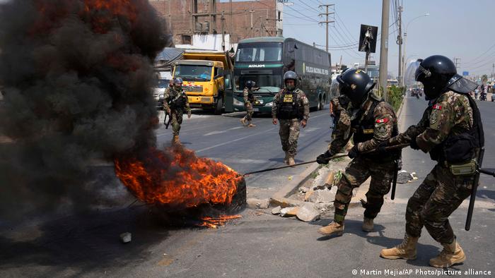 Policías remueven llantas incendiadas en la carretera, donde autobuses y camiones bloquean el tránsito desde y hacia Lima, la capital peruana.