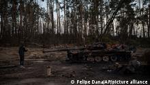 A man takes photos of a destroyed tank near Kyiv, Ukraine, Monday, April 4, 2022. (AP Photo/Fc