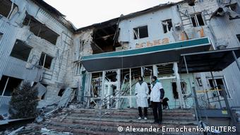 Двое мужчин в медицинских халатах стоят на ступенях разрушенной обстрелом больницы в Волновахе
