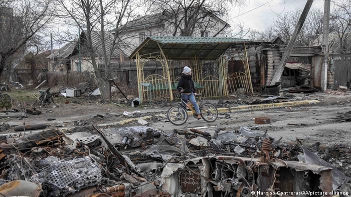 Жінка на велосипеді серед руйнувань на вулиці в Бучі після звільнення від військ РФ, фото 6 квітня 2022 року 