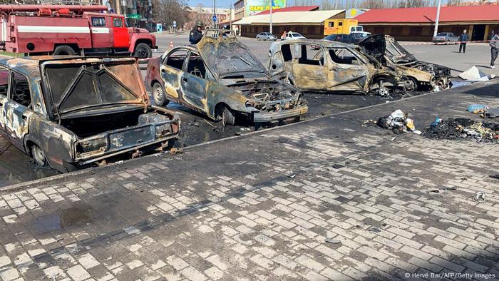 Vehicles damaged in a train station rocket attack, paint charred from their bodies and hoods, trunks and windows blown open or out