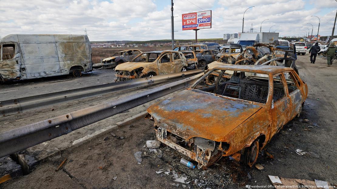 A foto mostra uma s&eacute;rie de autom&oacute;veis destru&iacute;dos, queimados devido a explos&otilde;es, &agrave; beira de uma estrada pr&oacute;xima &agrave; cidade de Bucha, na Ucr&acirc;nia.