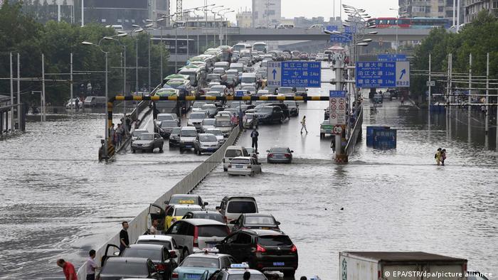 People walk in floodwater as many cars line up on a viaduct after the street was flooded due to heavy rainfalls in downtown Wuhan city
