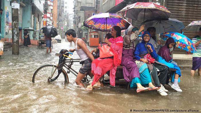 Passengers sit on a rickshaw van through flooded streets during a heavy downpour in Dhaka, Bangladesh