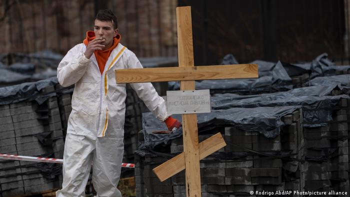 图为去年一名公墓工人在乌克兰乱葬坑识别在战争中遇难的平民。