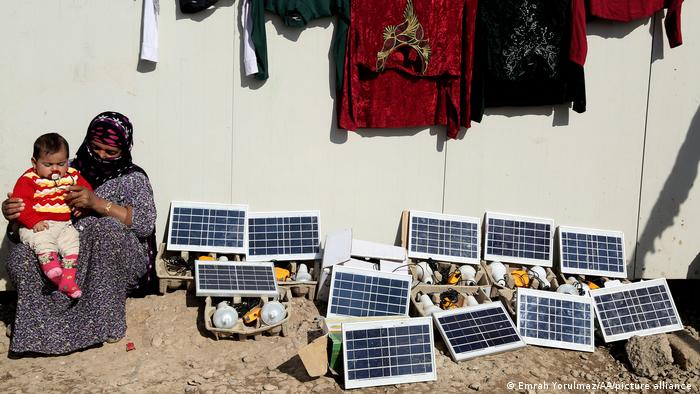 A woman and her child sit near a collection of small solar panels in a refugee camp in Erbil, Iraq