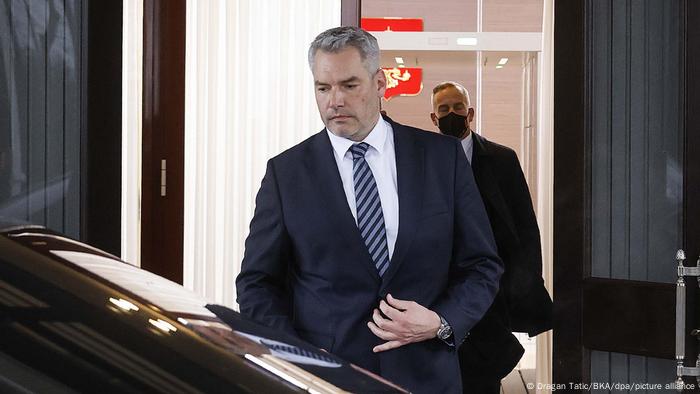 Austrian Chancellor Karl Nehammer gets into an awaiting vehicle after a meeting with Russian President Vladimir Putin as a man wearing a mask follows him