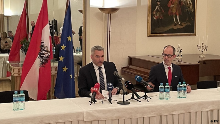 Austrian Chancellor Karl Nehammer at a press conference in Moscow in front of Austrian and EU flags; beside him is another official