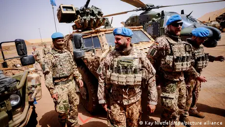 Armed German men wear blue berets and light-hued camouflage in a desert environment 