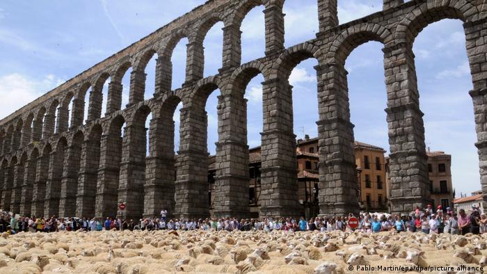 People stand in front of a massiv stone aqueduct