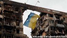 Zerstörter Wohnblock in Mariupol, von dem eine durchlöcherte ukrainische Fahne flattert