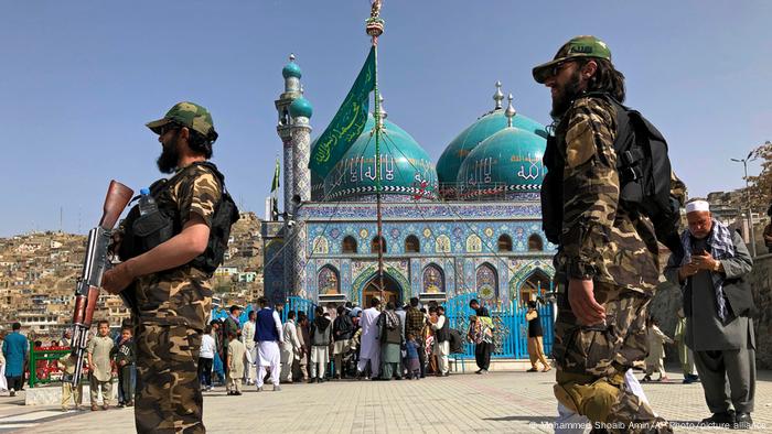 Men raise an Islamic flag during celebrations of Nowruz, the Persian new year, as Taliban soldiers stand guard