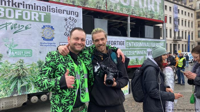 Un homme dans une citation sportive noire avec de grandes et petites feuilles de mauvaises herbes se tient avec un autre homme