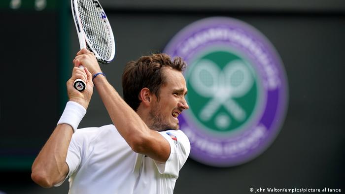 Tennis player Daniil Medvedev raising his racket with the Wimbledon logo behind him