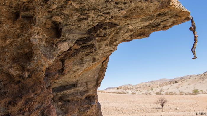 A human-like figure hangs from a cliff