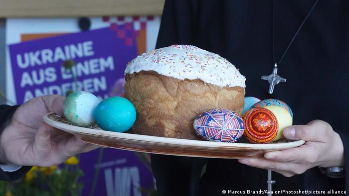 A person carries a plate with colored Easter eggs and a glazed Easter cake