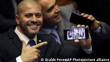 Deputy Daniel Silveira, who was elected to his first term representing the Social Liberal Party from where President Jair Bolsonaro mounted his campaign, points to his phone showing an image spoofing the jailed President former President Luiz Inacio Lula da Silva, during a swearing-in ceremony in the Chamber of Deputies, in Brasilia, Brazil, Friday, Feb. 1, 2019. (AP Photo/Eraldo Peres)
